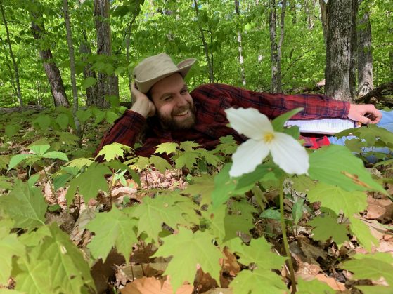 Nick Weld smiles next to a trillium flower