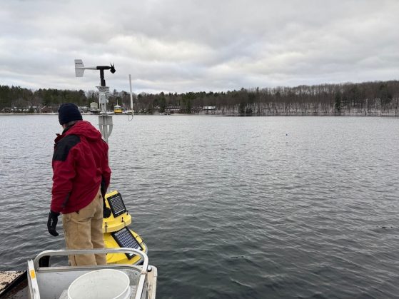 Man standing on a boat that is idling in a bay next to a big yellow buoy