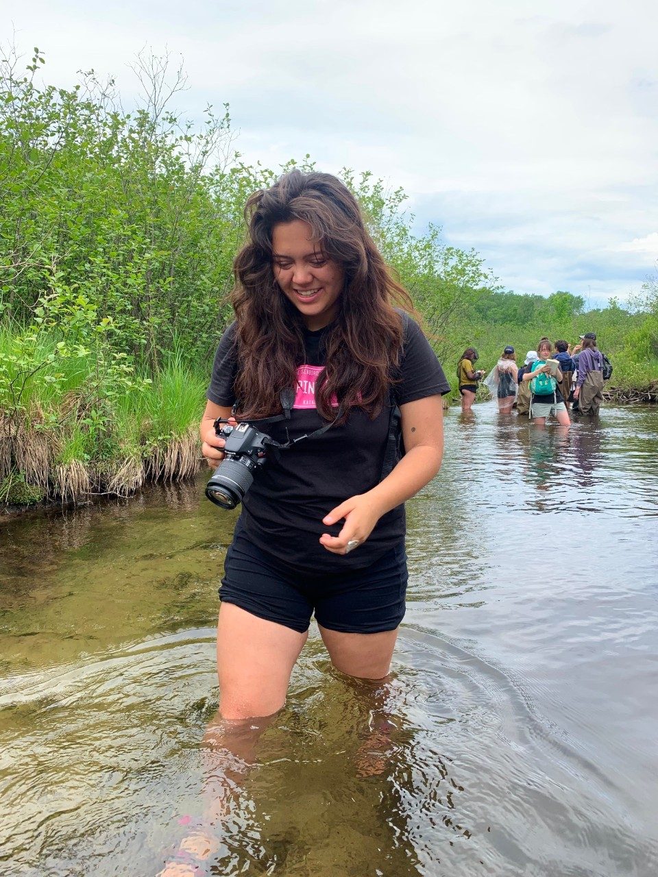Woman holds camera and wades through river