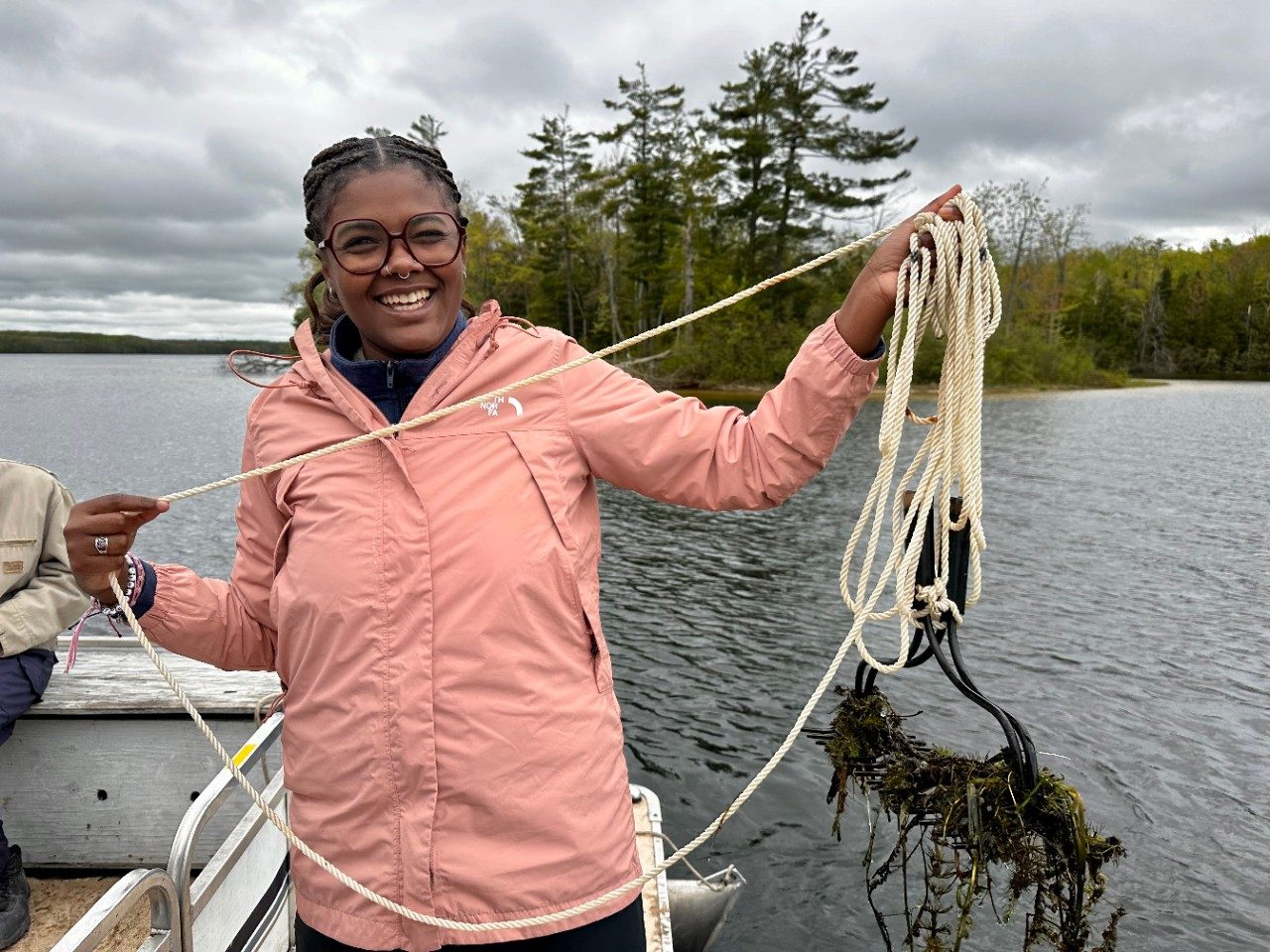 Person holding a rope with a rake attached at the end, on a boat in the water