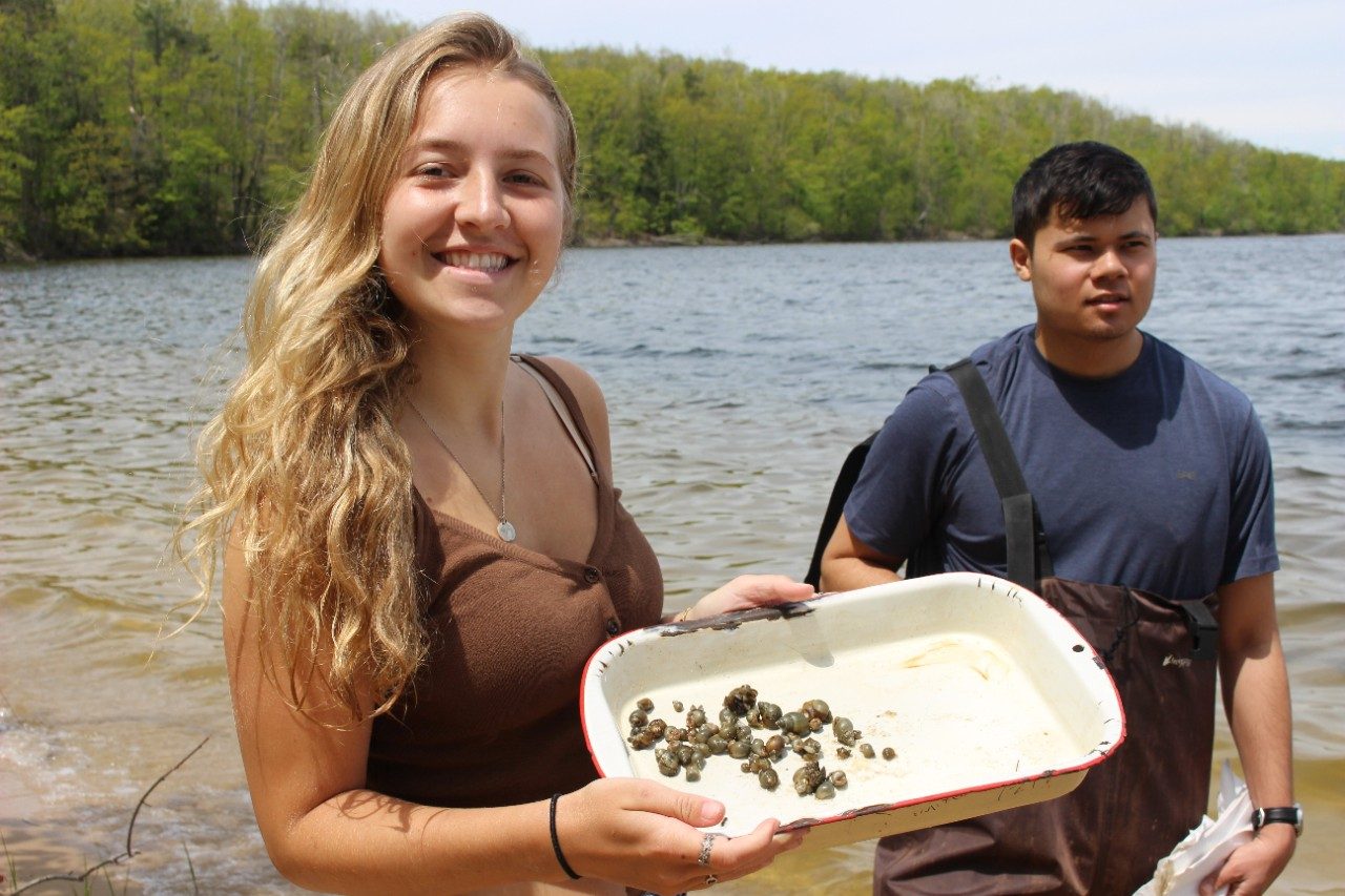 Person holding a pan with snails along a lake