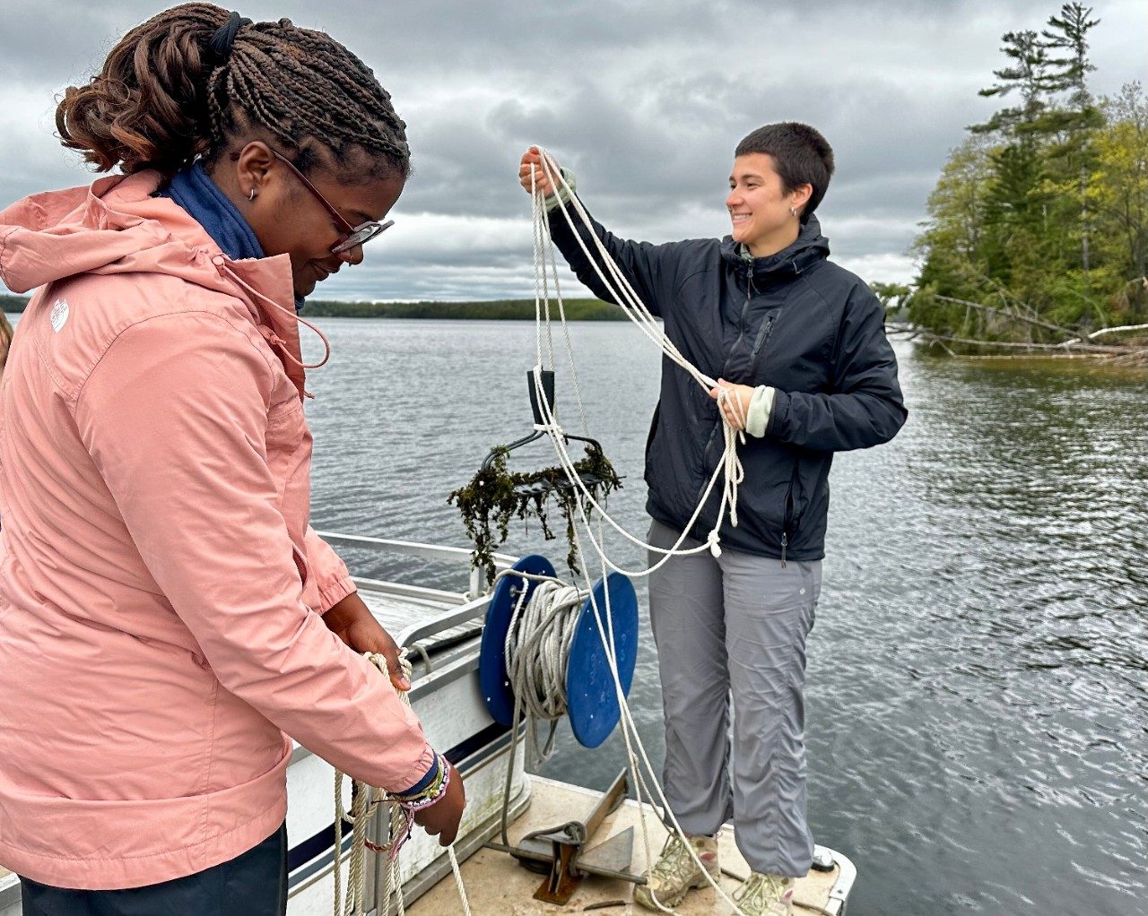 Person holding a rope with a rake attached at the end, on a boat in the water