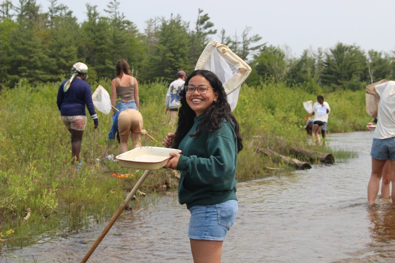 Woman standing a river holding a net and smiling at the camera