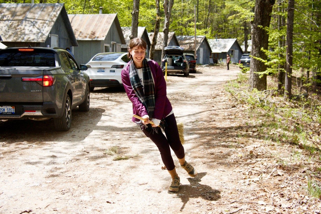 Woman dancing on broom outside of cabins in a forest