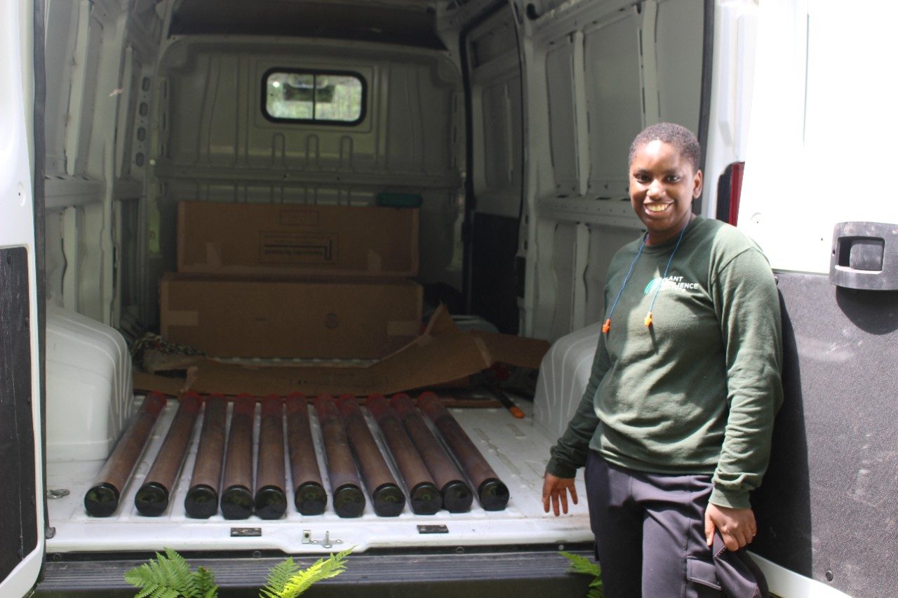 Person posing next to tubes full of soil in a van
