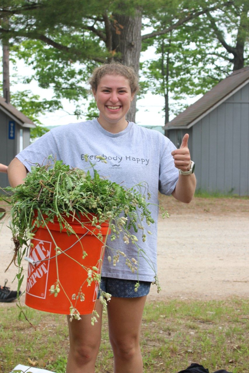 Person gives a thumbs up while holding a bucket of weeds