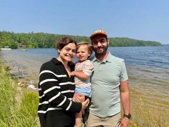 Family of three posing for a photo together along a lake