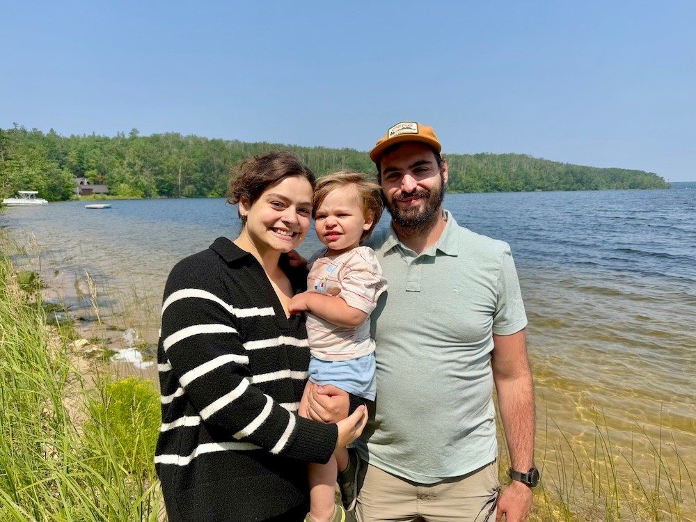 Family of three posing for a photo together along a lake