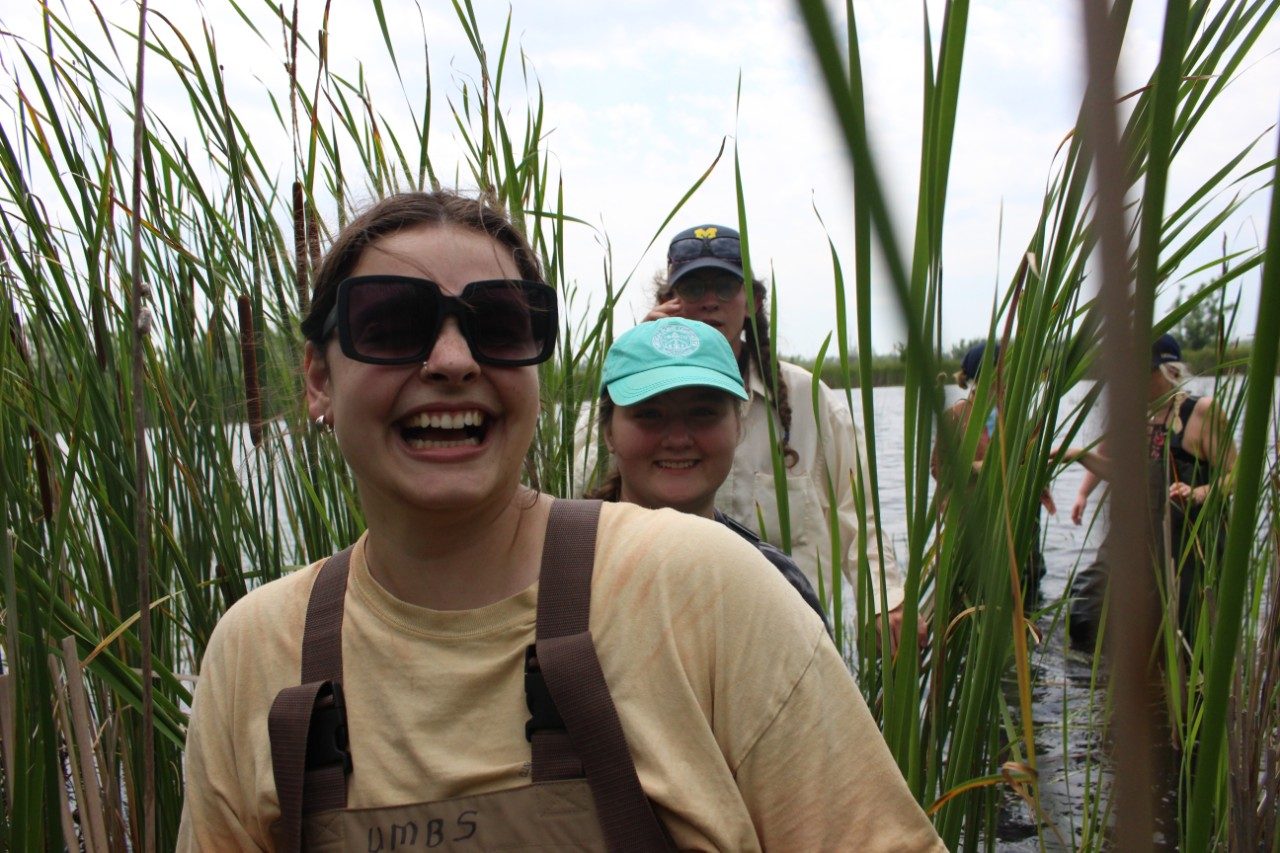 Person wearing waders and smiling in a marsh