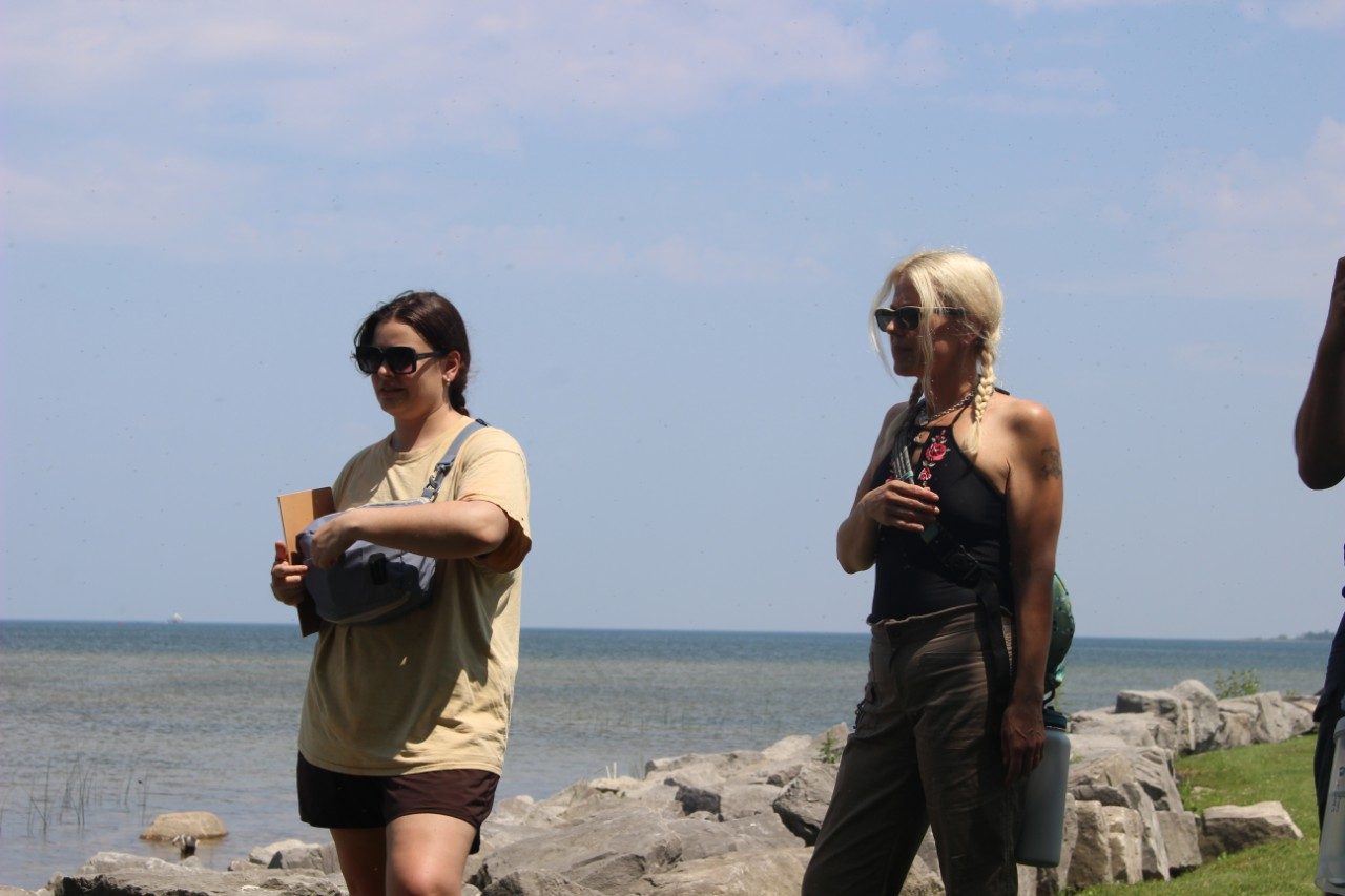 People standing along a lakeshore and taking notes