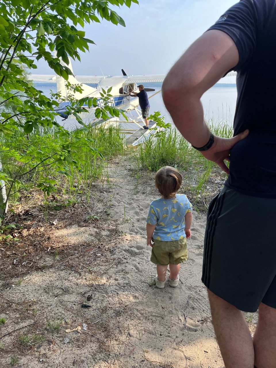 Child watches people board a seaplane on a lake shoreline