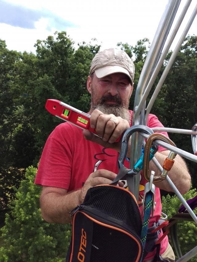 Man safely strapped on to a tower that he is climbing in a forest