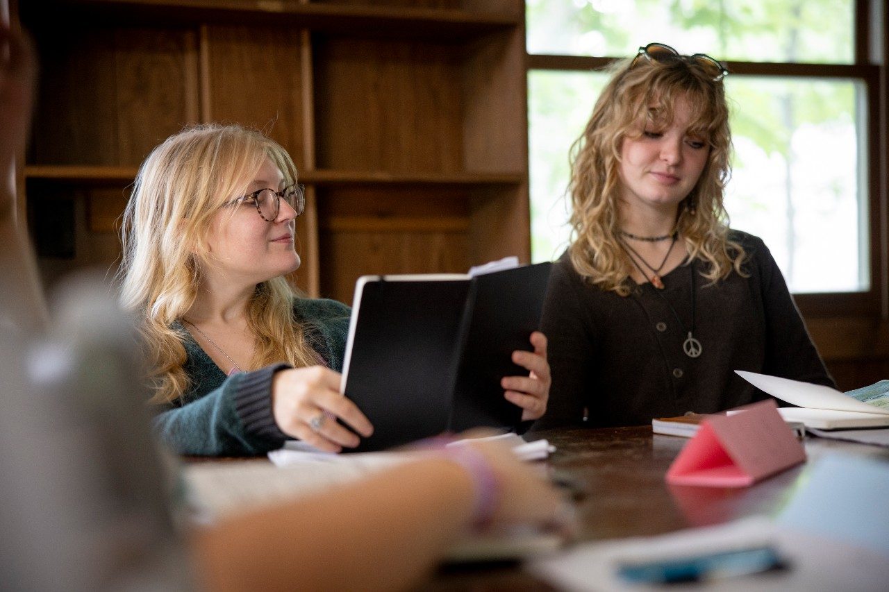 Two students sitting at a table in a classroom looking at books