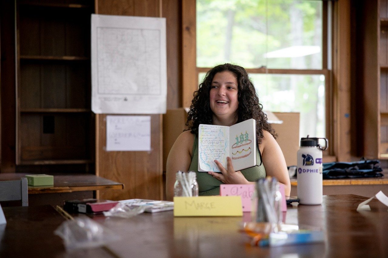 Woman holds up a notebook to show drawing