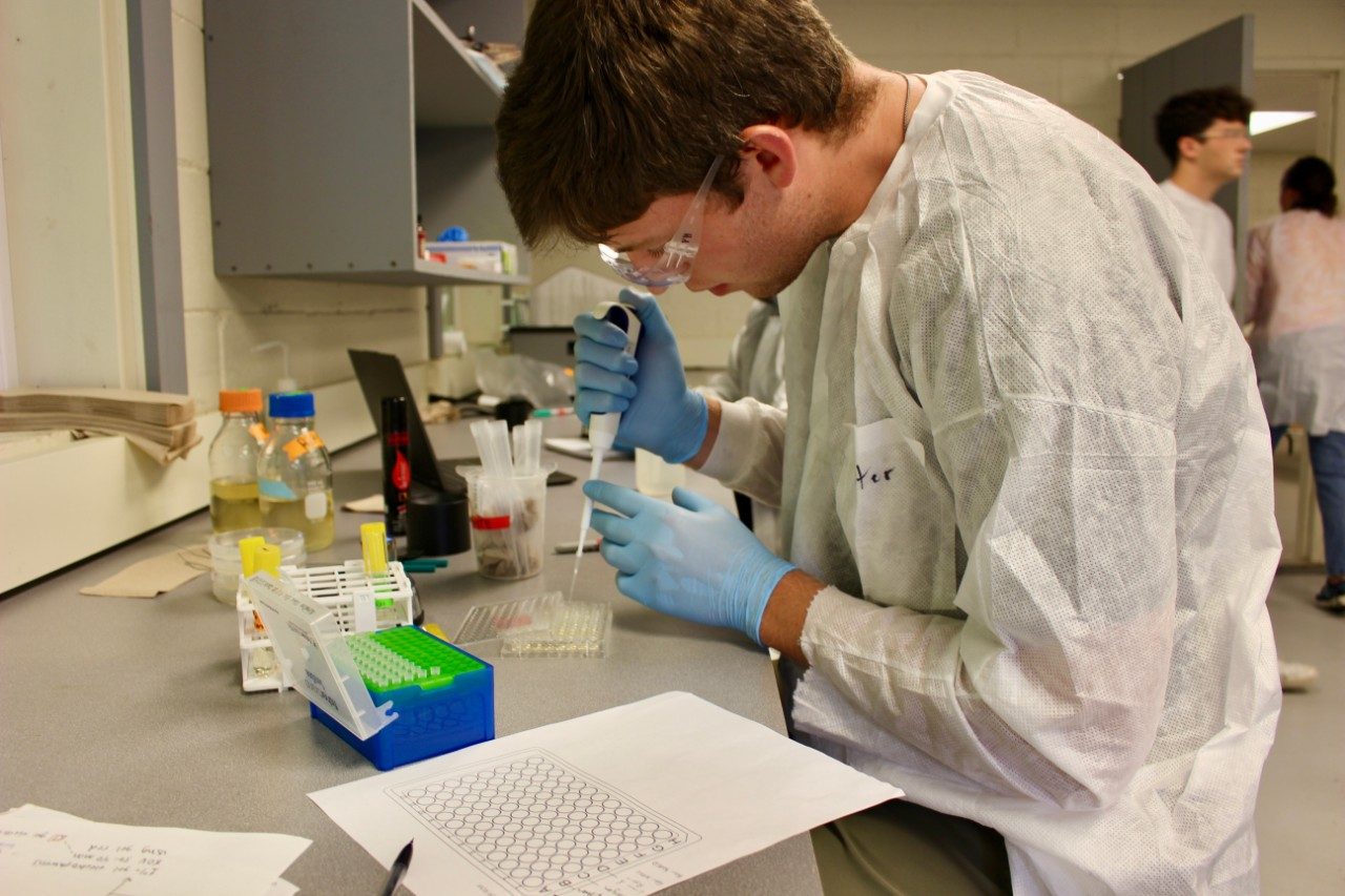 Student wearing protective lab gear working with lab equipment
