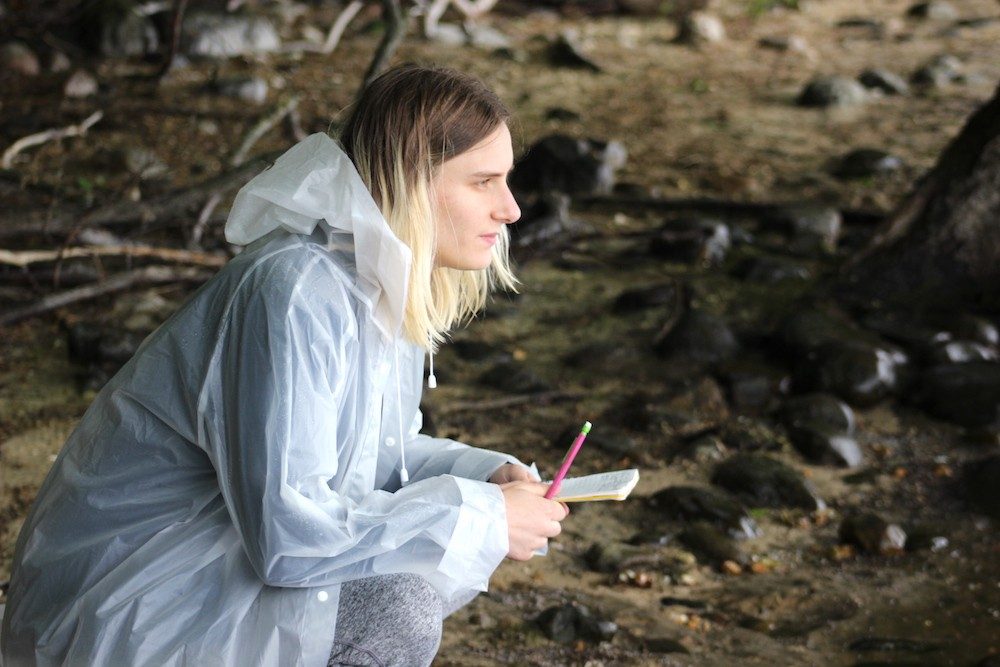 Person in rain gear sitting on the shore of a lake
