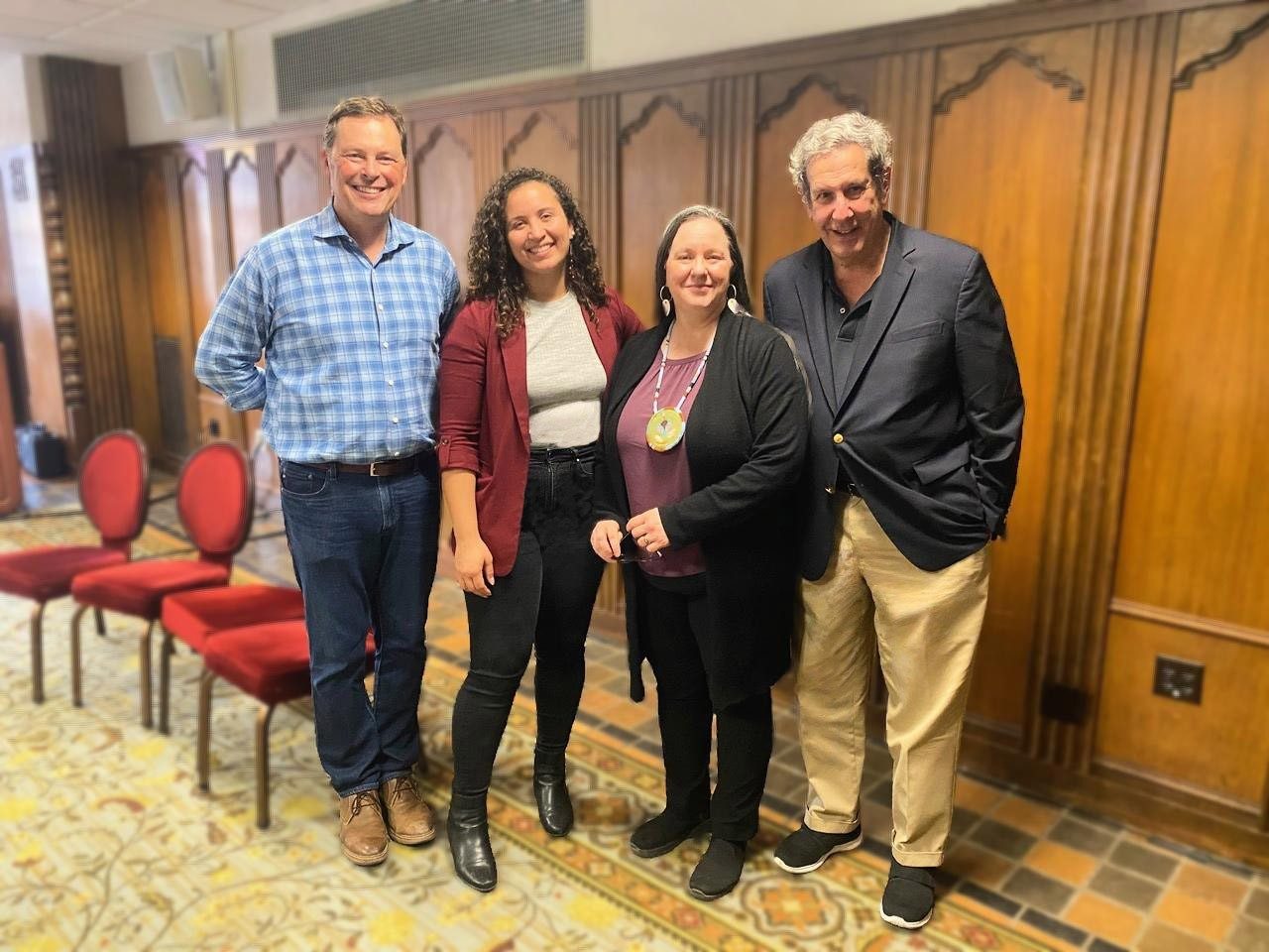 Four people stand in a row next to each other in a room. 