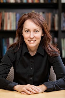 Anna Kirkland stands in a black shirt in front of books