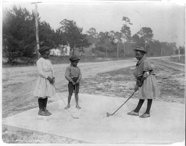 Young children in a black and white photograph playing mini golf